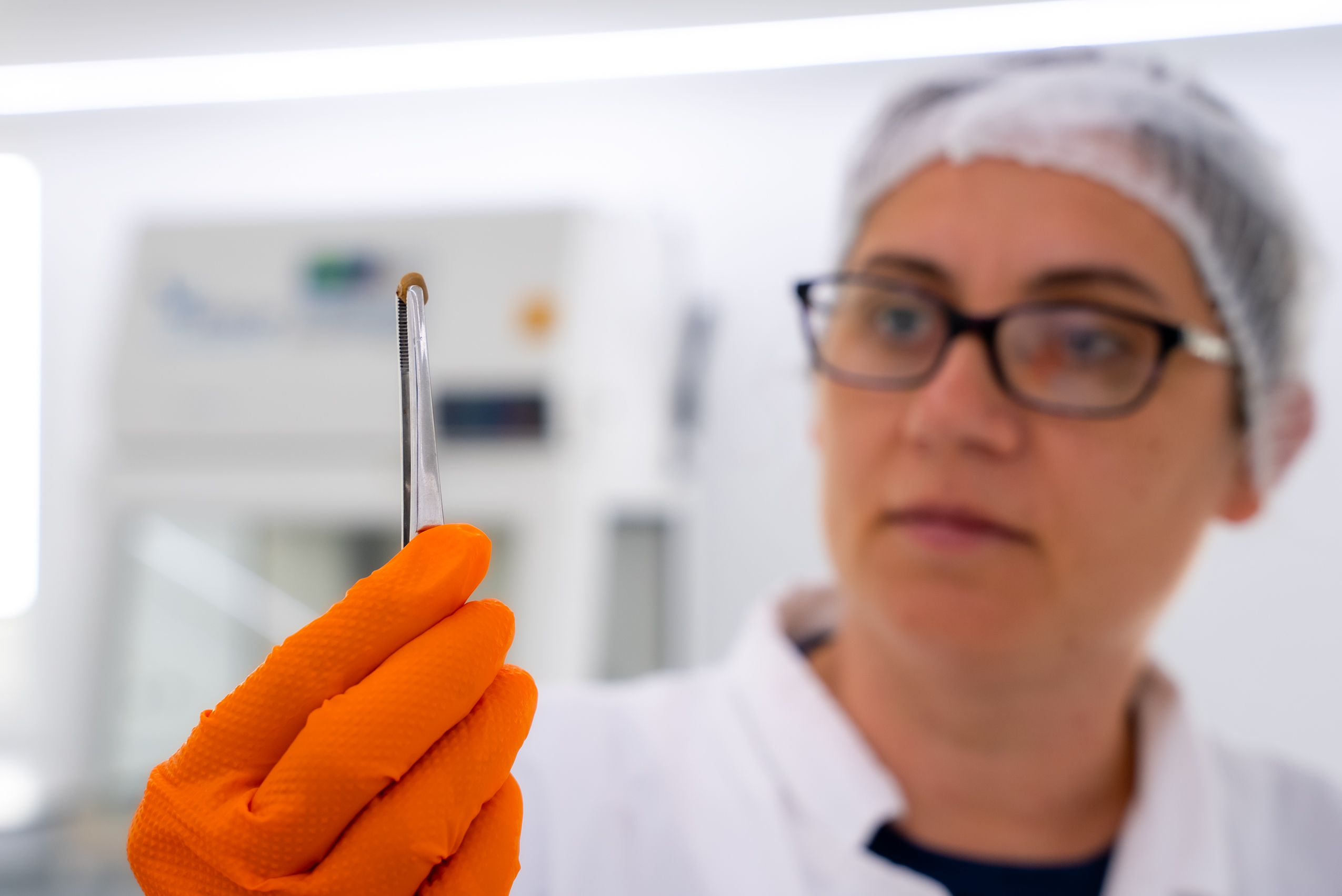 Mujer coge semilla con pinzas en laboratorio